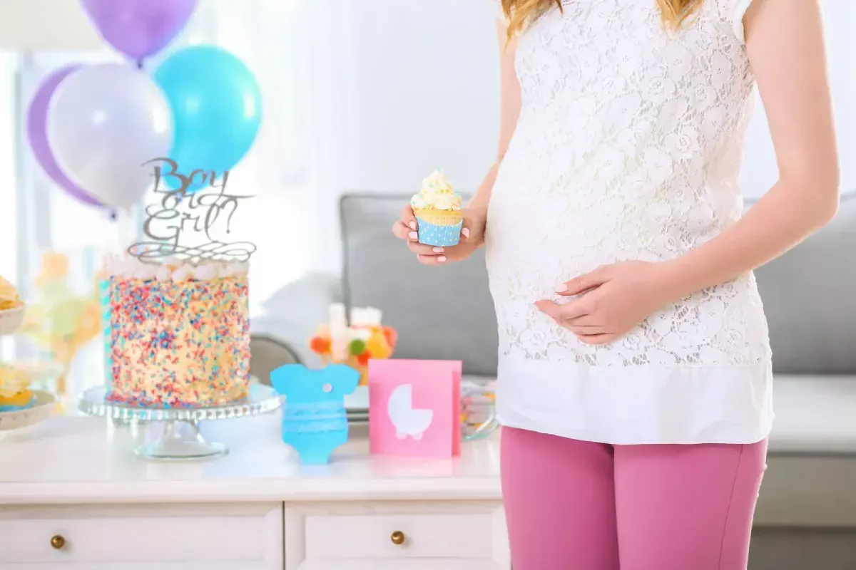 Pregnant woman at gender reveal party holding a cupcake.