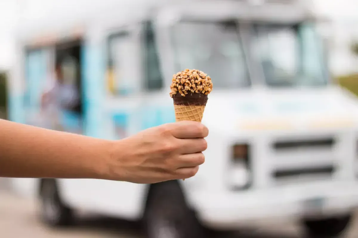 Hand holding an ice cream cone in front of a food truck.